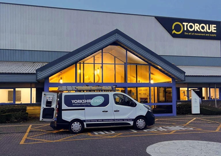 A white van with Yorkshire Pro Window Cleaning branding parked outside a building with a large sign featuring the Torque logo