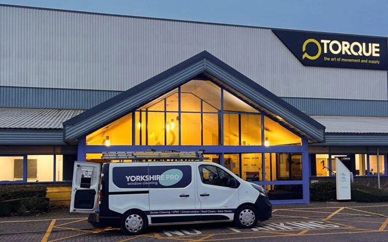 A white van with Yorkshire Pro Window Cleaning branding parked outside a building with a large sign featuring the Torque logo